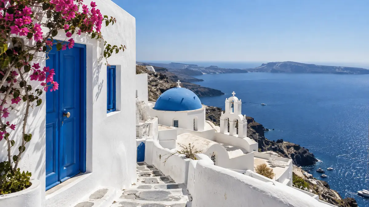 Λευκά κυκλαδίτικα σπίτια με μπλε πόρτες και τρούλο, με θέα στο Αιγαίο Πέλαγος